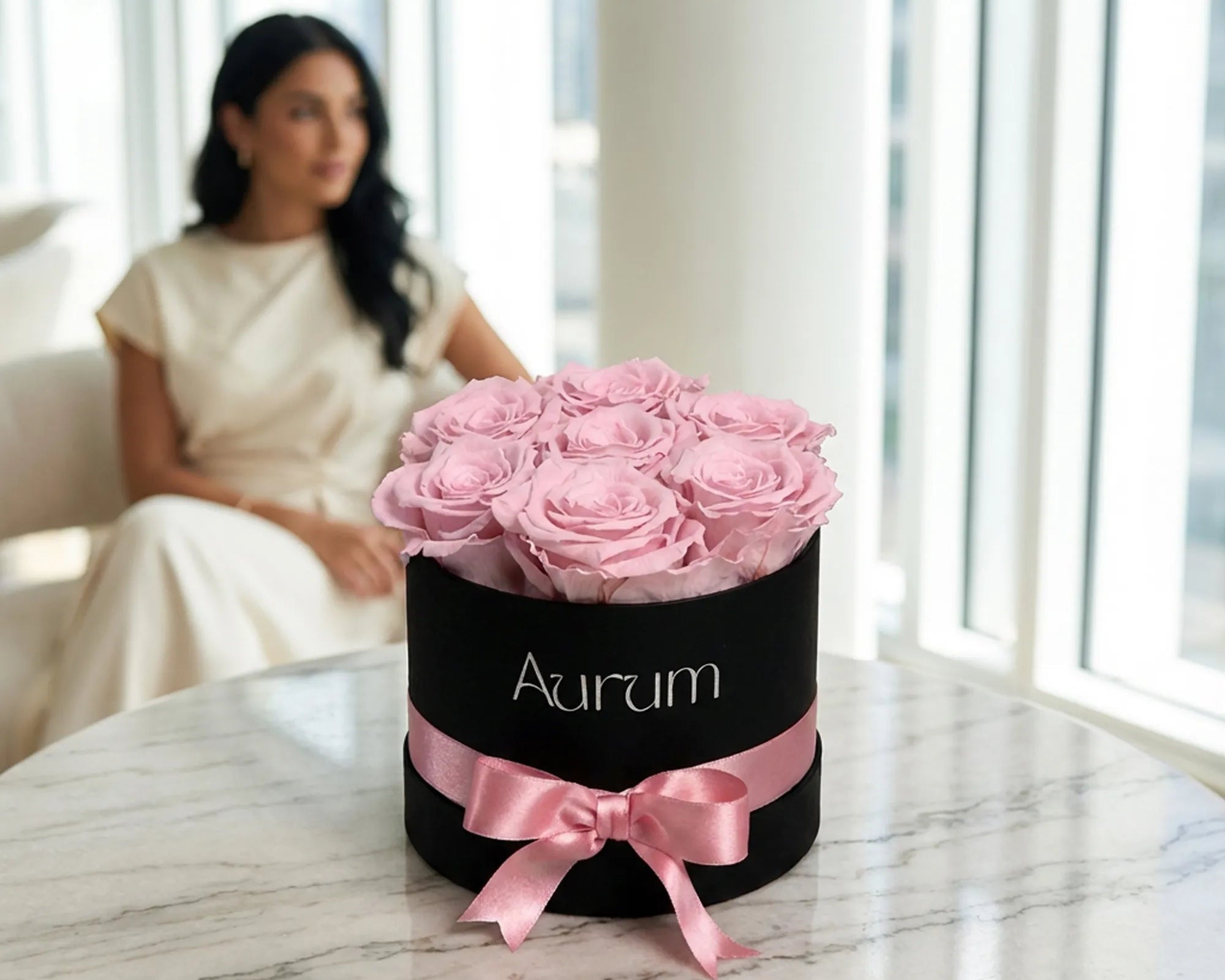 Black box with pink roses and a pink bow labeled 'Aurum' on a marble surface with a blurred background.